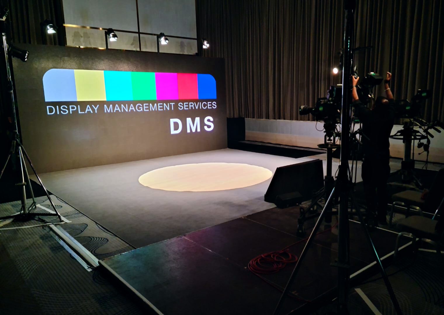 Stage set with the Display Management Services logo on the LED wall and broadcast cameras ready